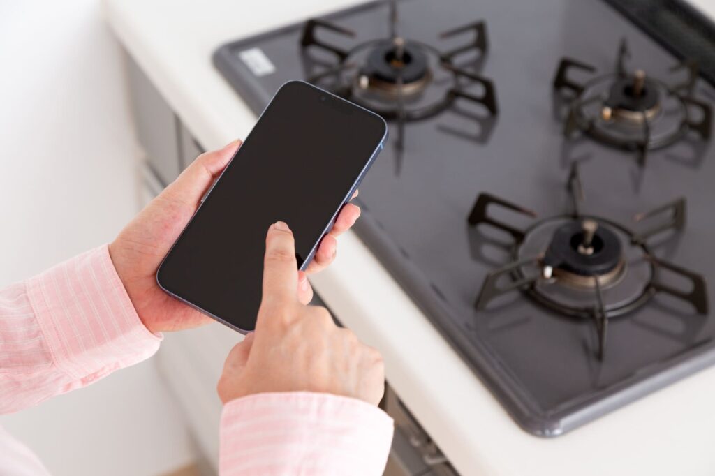 ガスコンロの前でスマホを構える女性